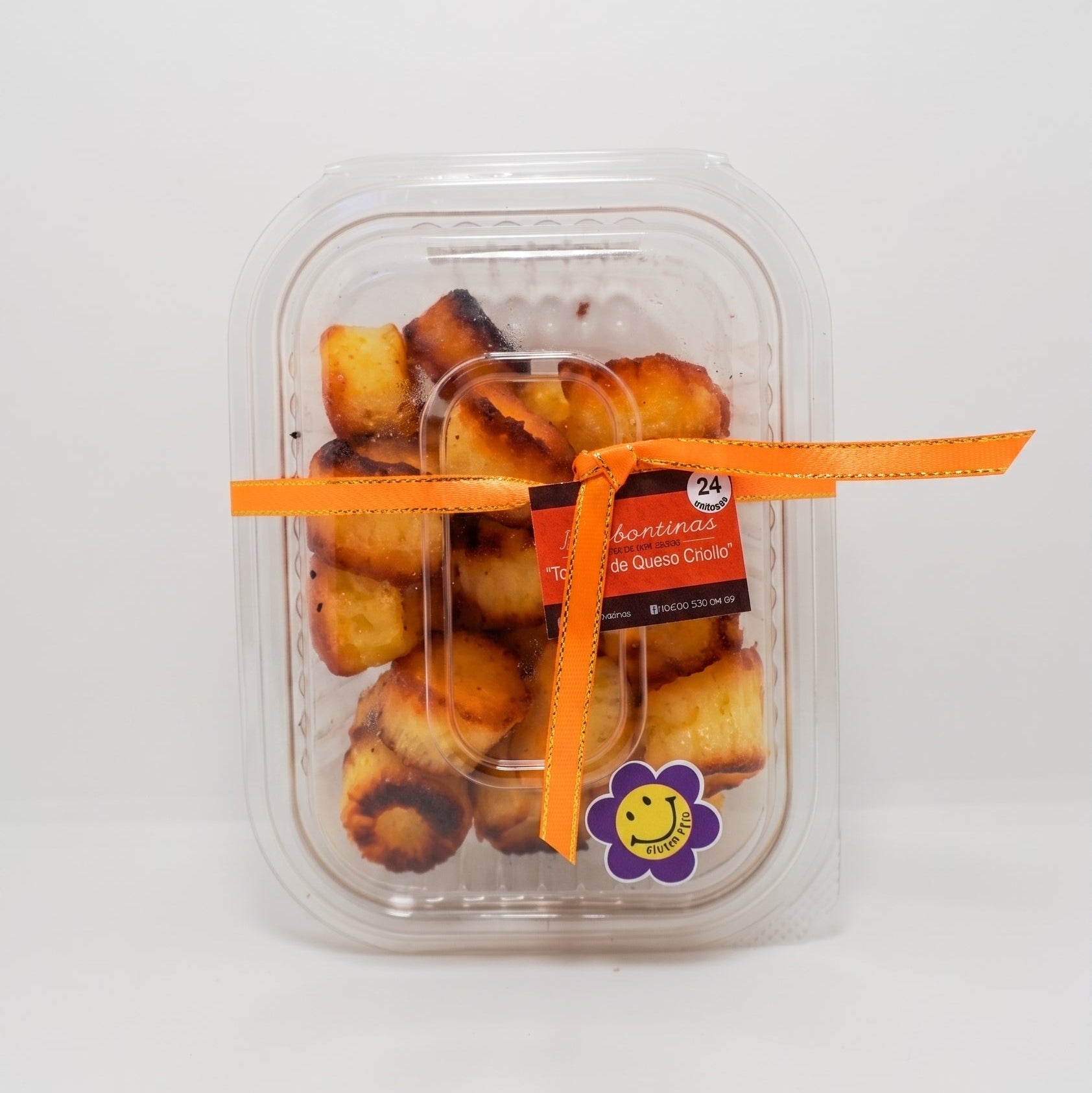A clear plastic clamshell container filled with golden-brown baked pastries, tied with a bright orange ribbon and a small flower-shaped sticker, on a plain white background.